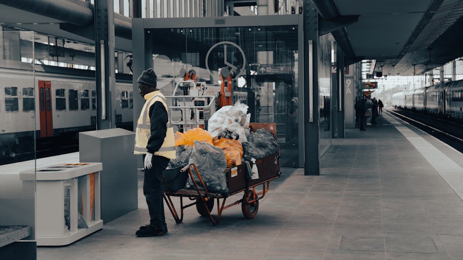 A photograph displays a pile of various waste materials placed on a paved outdoor surface, likely a driveway or pavement area. In the foreground, there are several black trash bags with a matte finish